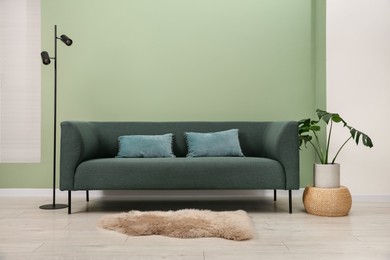 Photo of Stylish sofa with pillows, houseplant and lamp near green wall indoors