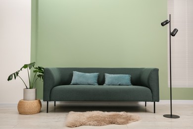 Photo of Stylish sofa with pillows, houseplant and lamp near green wall indoors