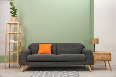 Photo of Stylish sofa with pillow, side table, shelving unit and houseplant near green wall indoors