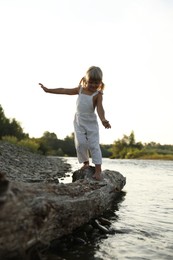 Cute little girl walking along tree trunk near river. Child enjoying beautiful nature