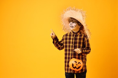 Funny boy with pumpkin bucket dressed like scarecrow pointing at something on yellow background, space for text. Halloween celebration