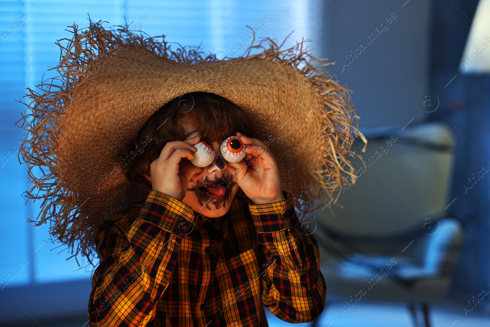 Photo of Boy with decorative eyeballs dressed like scarecrow indoors at night. Halloween celebration