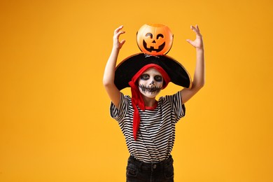 Photo of Funny boy with pumpkin bucket dressed like pirate on yellow background. Halloween costume