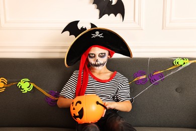 Photo of Funny boy with different Halloween decor dressed like pirate on sofa indoors