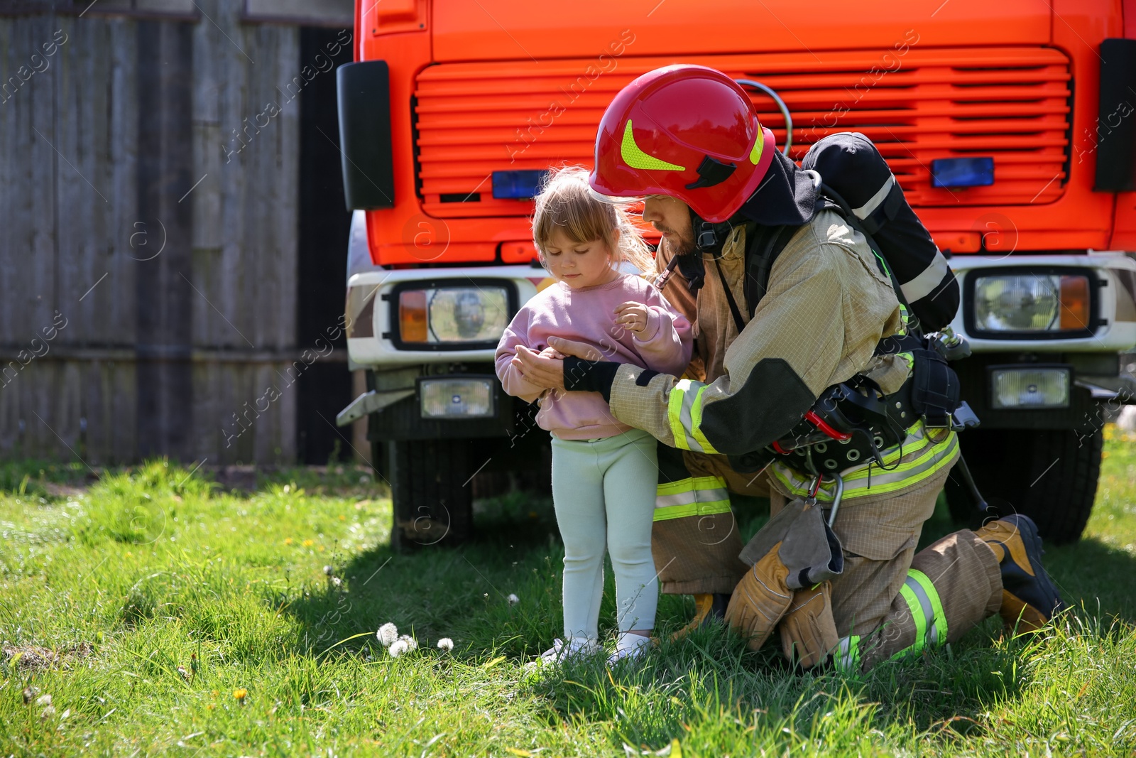 Photo of Firefighter in uniform with rescued little girl near fire truck outdoors. Save life