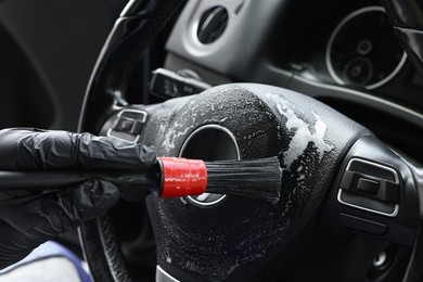 Photo of Man cleaning steering wheel with brush in car, closeup