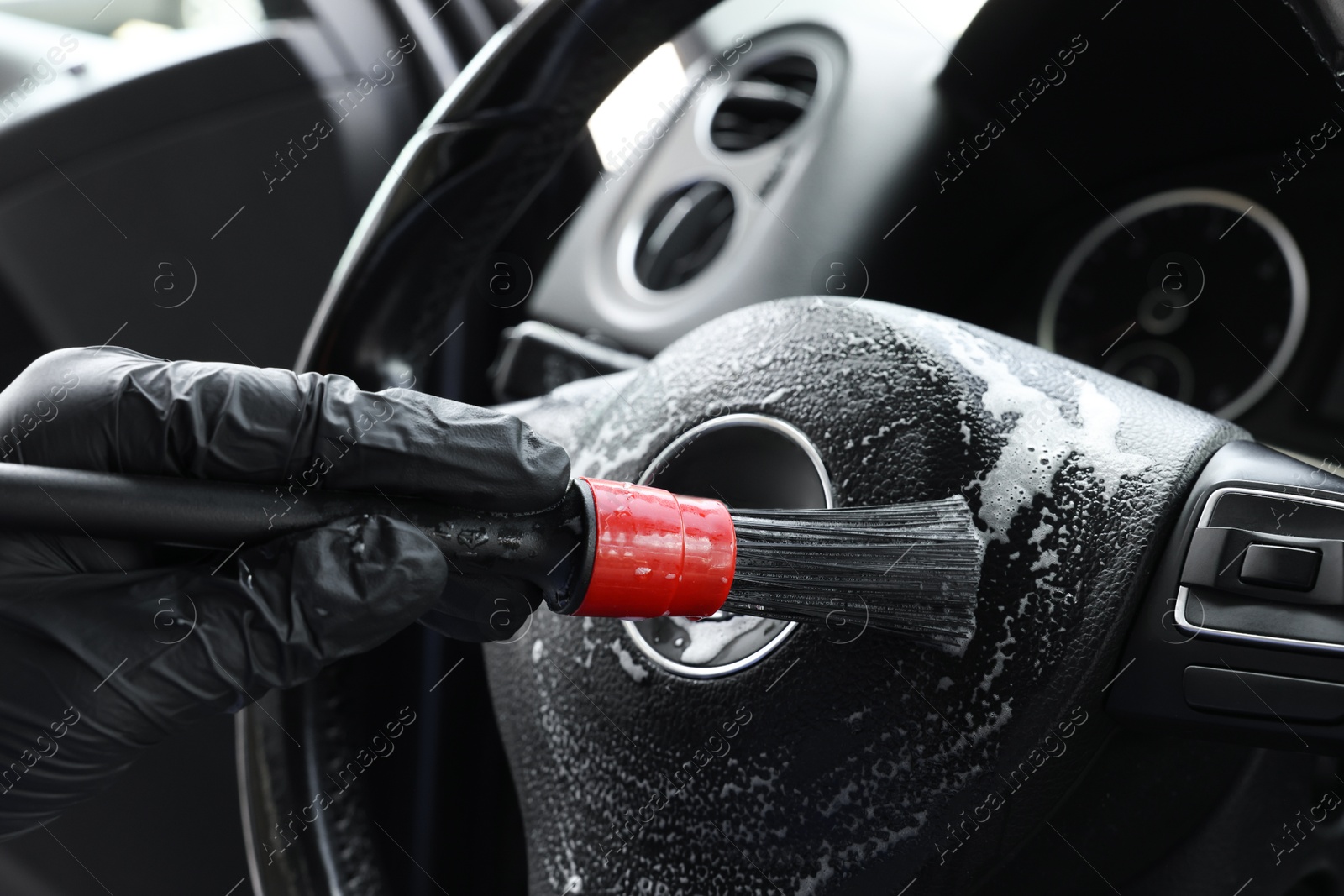 Photo of Man cleaning steering wheel with brush in car, closeup