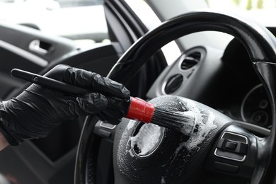 Man cleaning steering wheel with brush in car, closeup