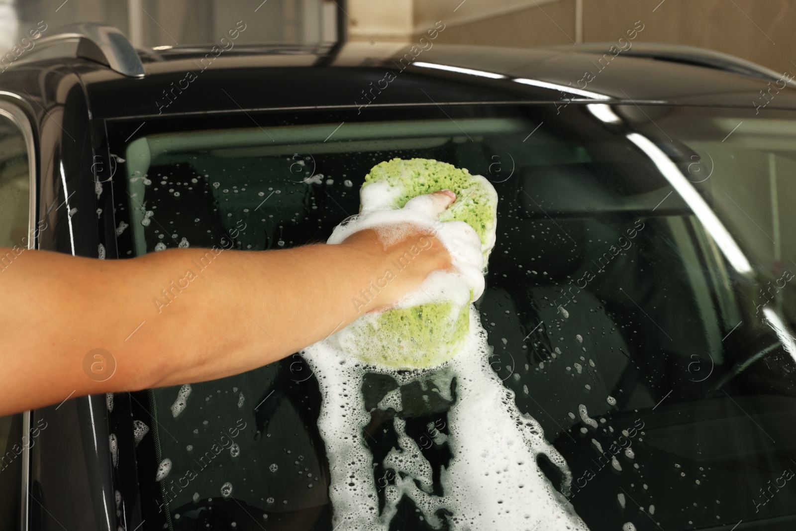 Photo of Man washing car windshield with sponge indoors, closeup