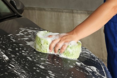 Man washing car hood with sponge indoors, closeup