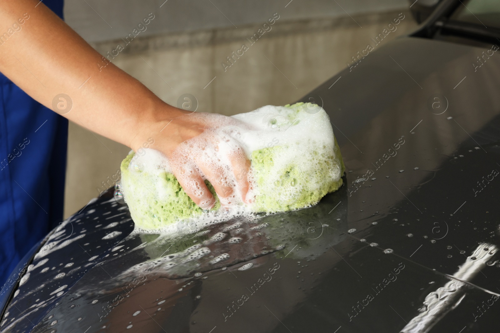 Photo of Man washing car hood with sponge indoors, closeup