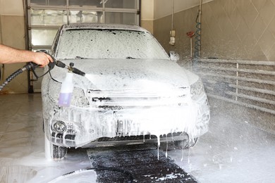 Man washing auto with high pressure water jet at car wash, closeup