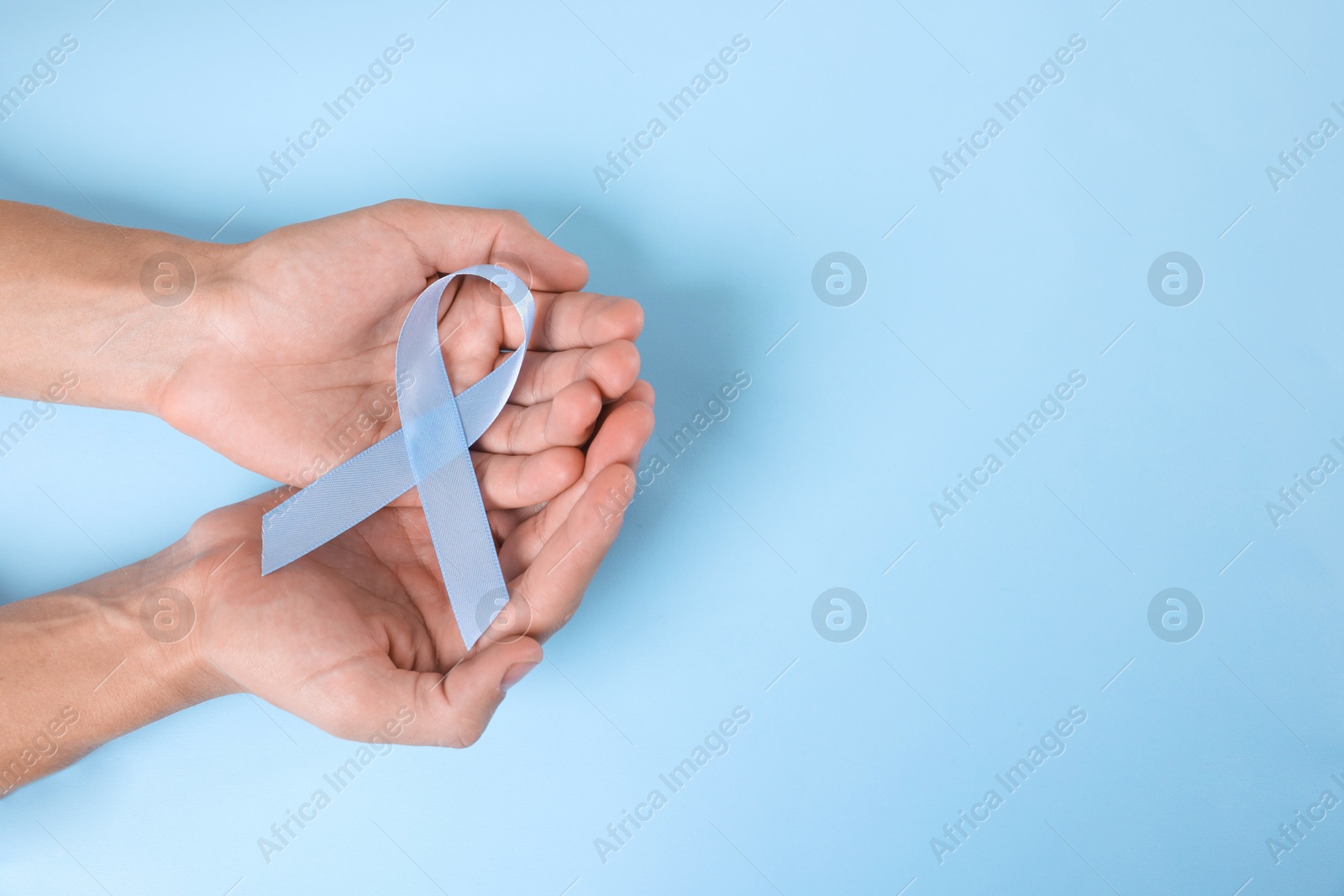 Photo of Prostate cancer awareness. Man with light blue ribbon as symbol of support on color background, top view. Space for text