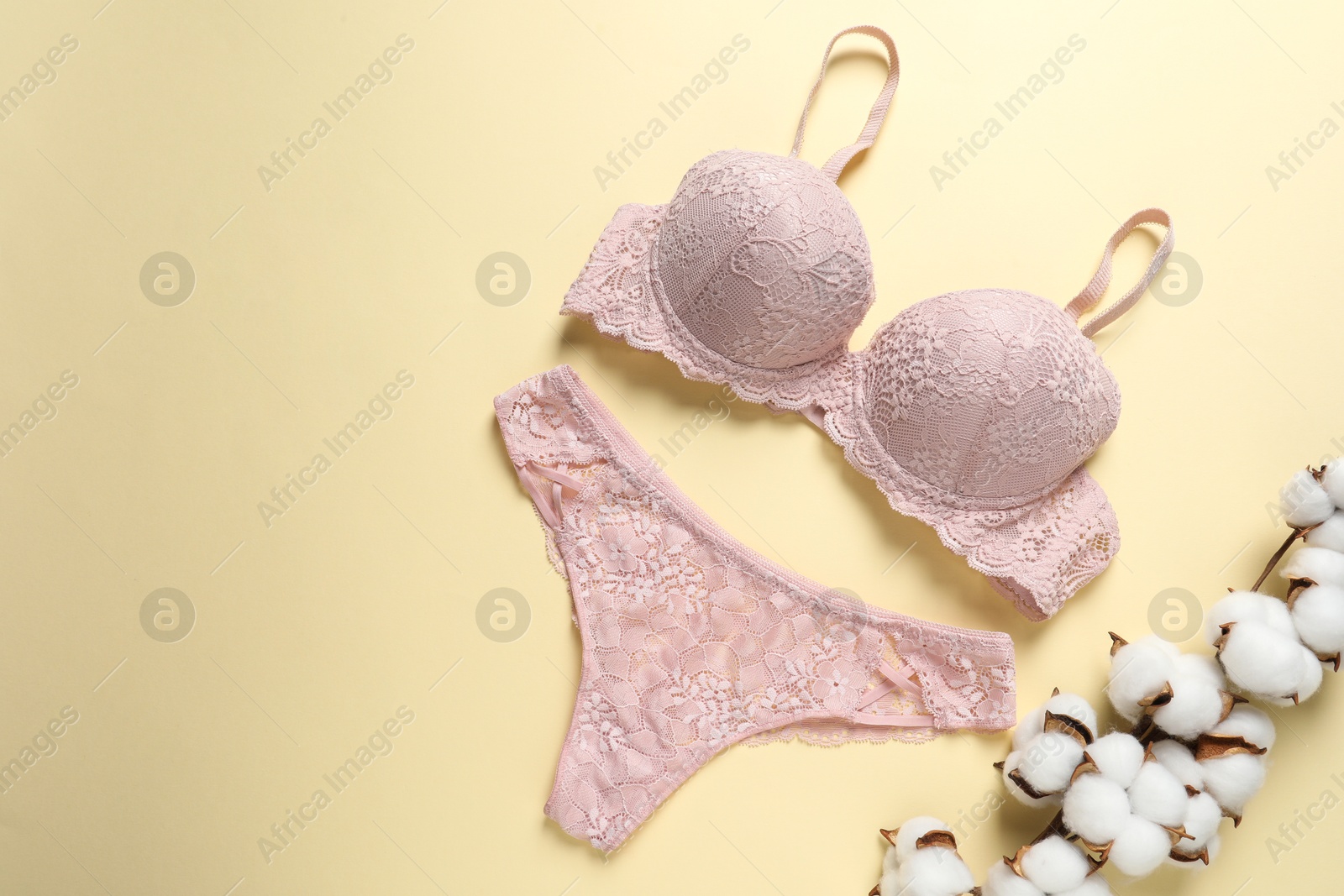 Photo of Elegant pink lace women's underwear and cotton flowers on beige background, top view. Space for text