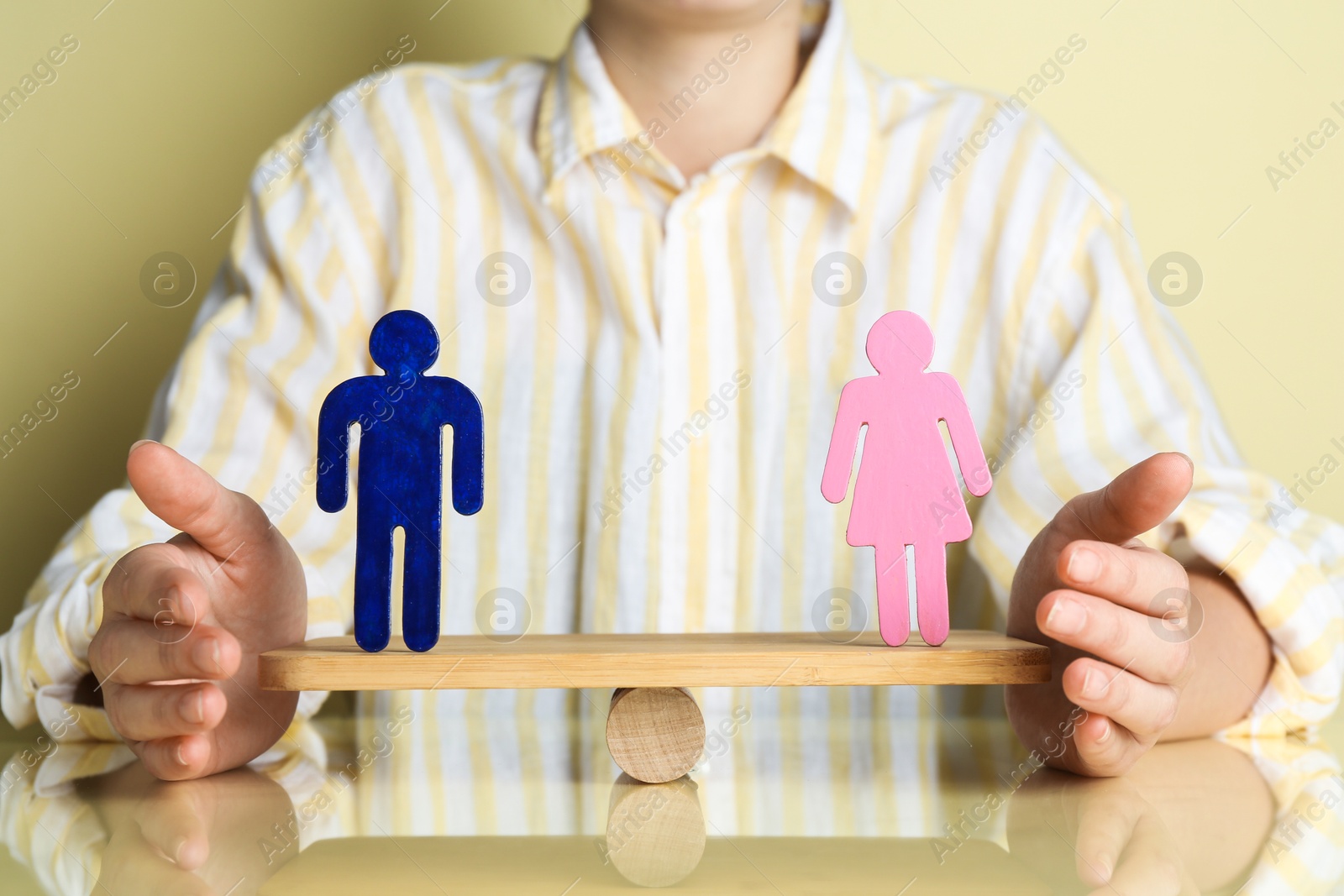 Photo of Gender equality concept. Woman with male and female figures on scales against light yellow background, closeup