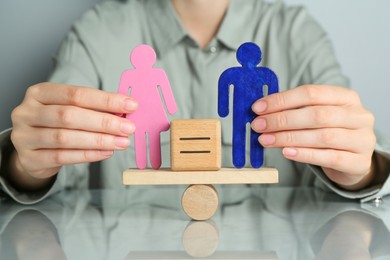 Gender equality concept. Woman with male and female figures on scales at grey table, closeup