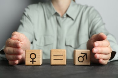 Photo of Gender equality concept. Woman with wooden cubes of male and female symbols at grey table, closeup