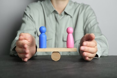 Photo of Gender equality concept. Woman with male and female figures on scales at dark table, closeup