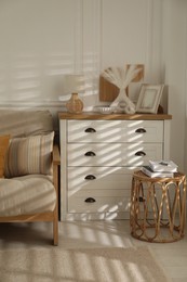 Photo of Sofa with soft pillows, chest of drawers, different decorative elements and side table indoors