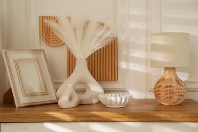 Photo of Beautiful decorative plants, vases, photo frame, ceramic bowl and lamp on wooden chest of drawers indoors