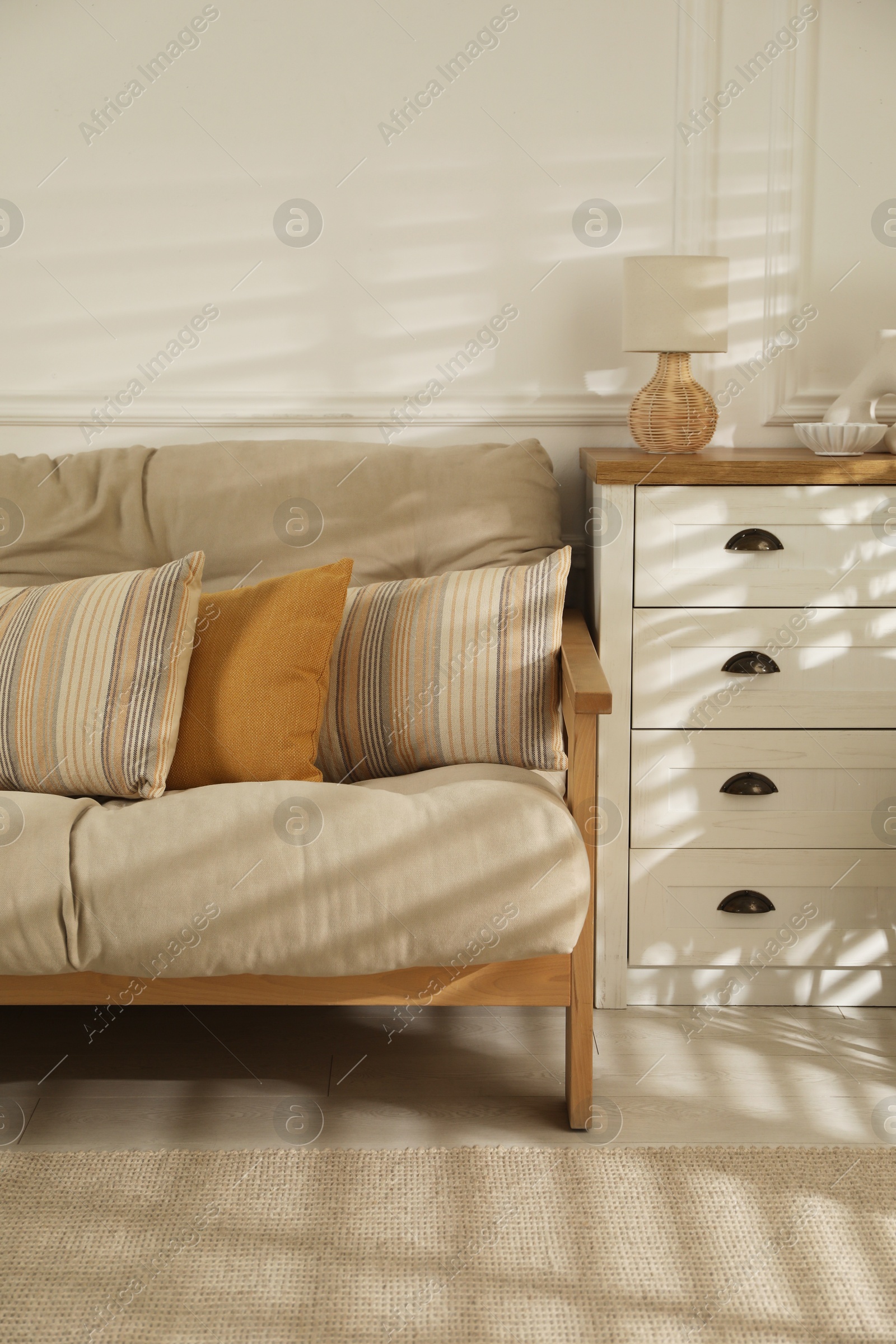 Photo of Sofa with soft pillows, chest of drawers and different decorative elements indoors