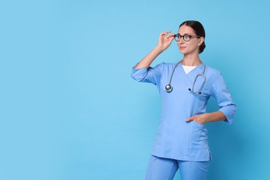 Nurse in medical uniform with stethoscope on light blue background, space for text