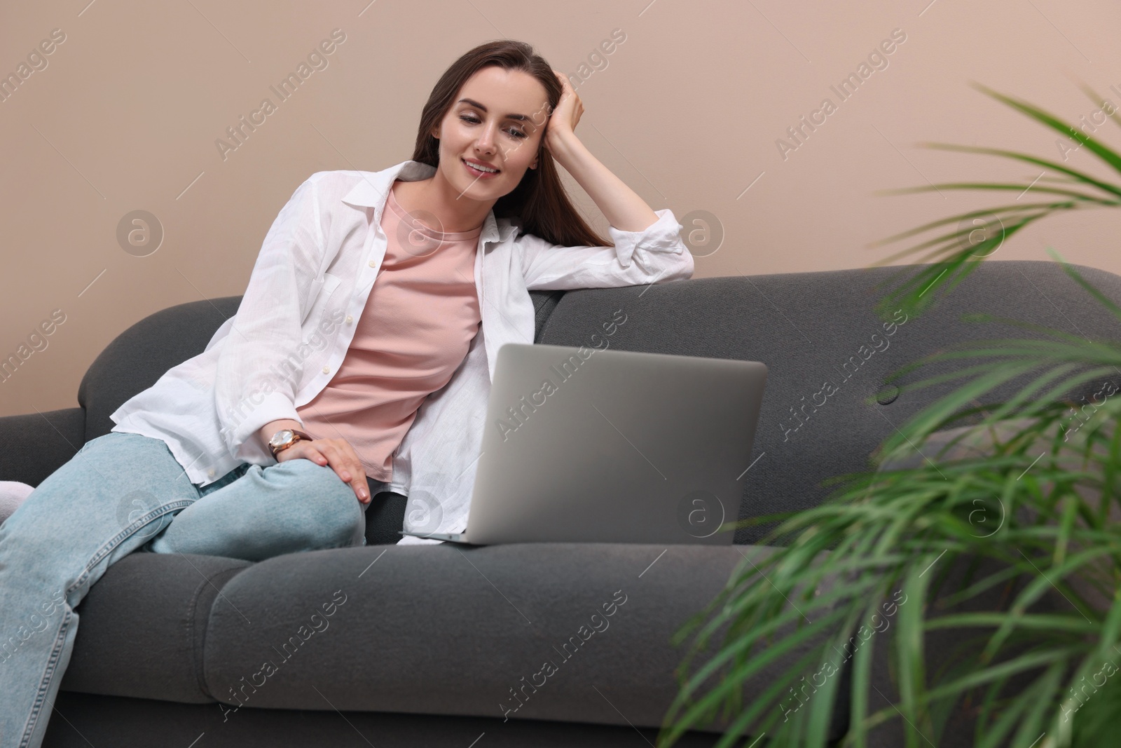 Photo of Smiling woman looking at laptop on sofa at home. Break time