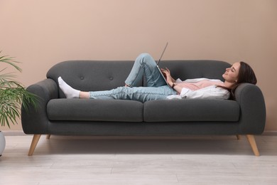 Smiling woman with laptop lying on sofa at home