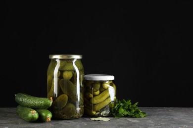 Photo of Tasty pickled cucumbers in jars and fresh ingredients on grey textured table. Space for text