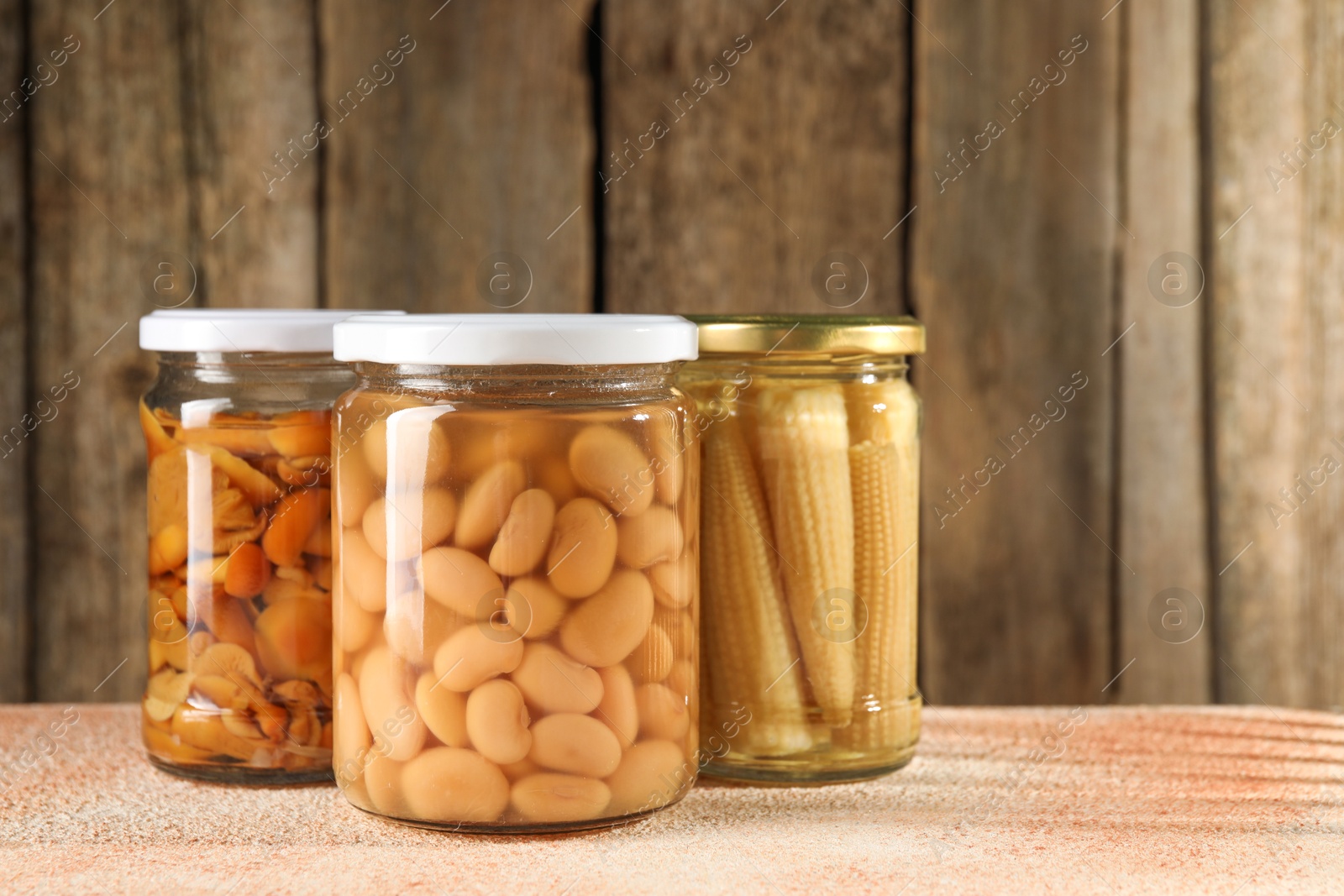 Photo of Different pickled products in jars on beige textured table