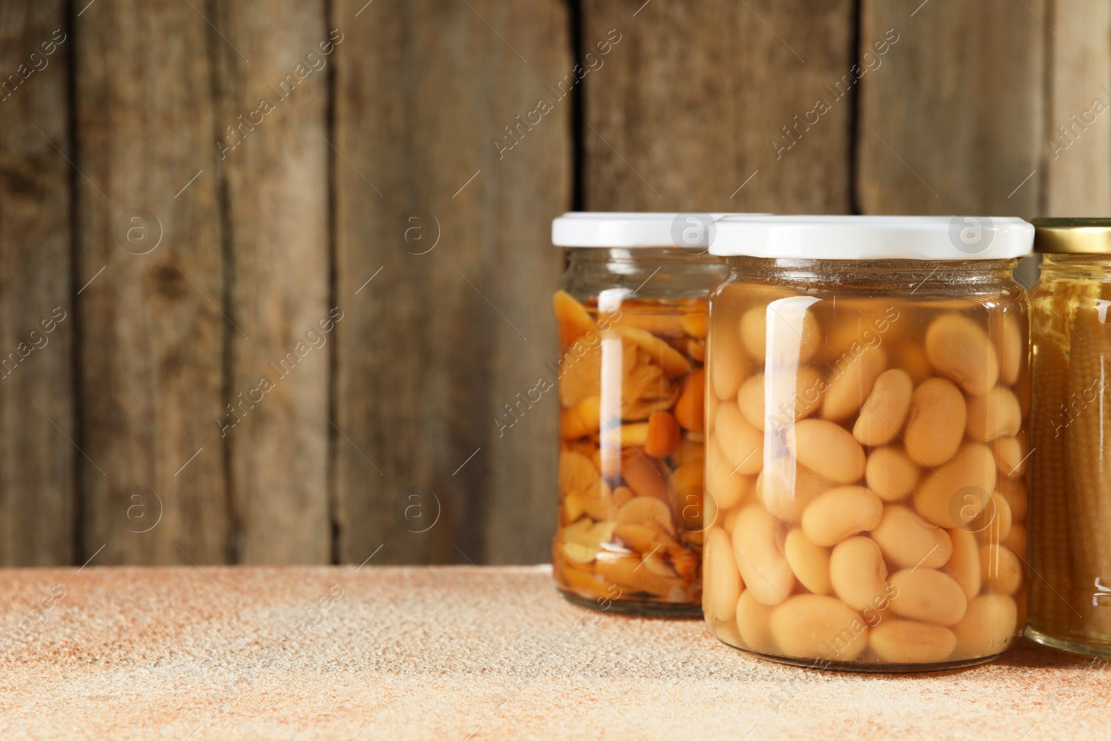 Photo of Different pickled products in jars on beige textured table, space for text