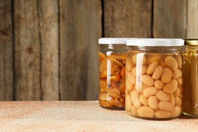 Photo of Different pickled products in jars on beige textured table, space for text