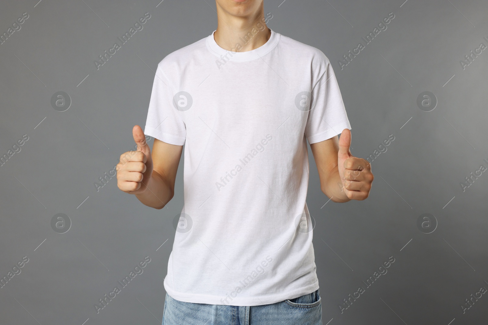 Photo of Teenage boy wearing white t-shirt and showing thumbs up on grey background, closeup