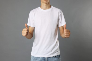 Photo of Teenage boy wearing white t-shirt and showing thumbs up on grey background, closeup