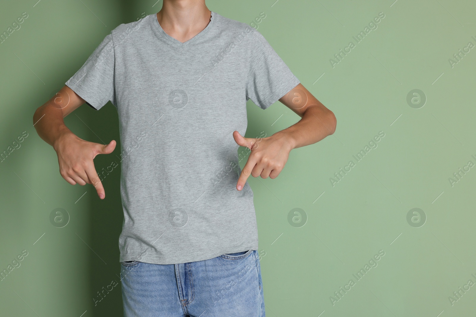 Photo of Teenage boy wearing light grey t-shirt on green background, closeup. Space for text