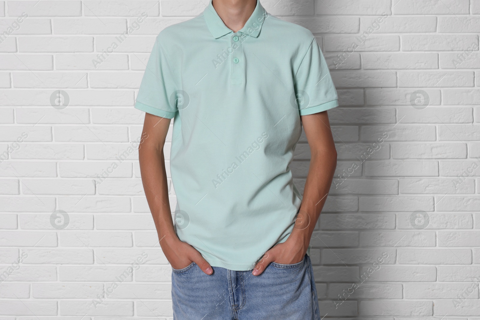 Photo of Teenage boy wearing light green t-shirt near white brick wall, closeup