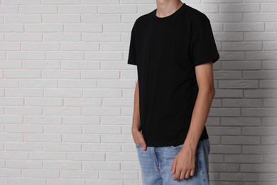 Photo of Teenage boy wearing black t-shirt near white brick wall, closeup. Space for text