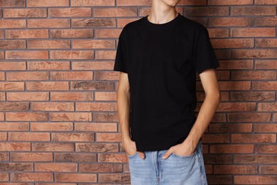 Photo of Teenage boy wearing black t-shirt near brick wall, closeup. Space for text