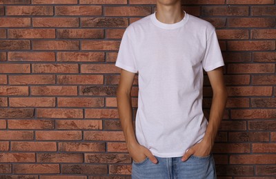 Photo of Teenage boy wearing white t-shirt near brick wall, closeup. Space for text