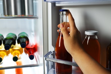 Woman taking bottle with drink from refrigerator, closeup