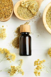 Photo of Tincture in bottle and helichrysum flowers on white wooden table, flat lay