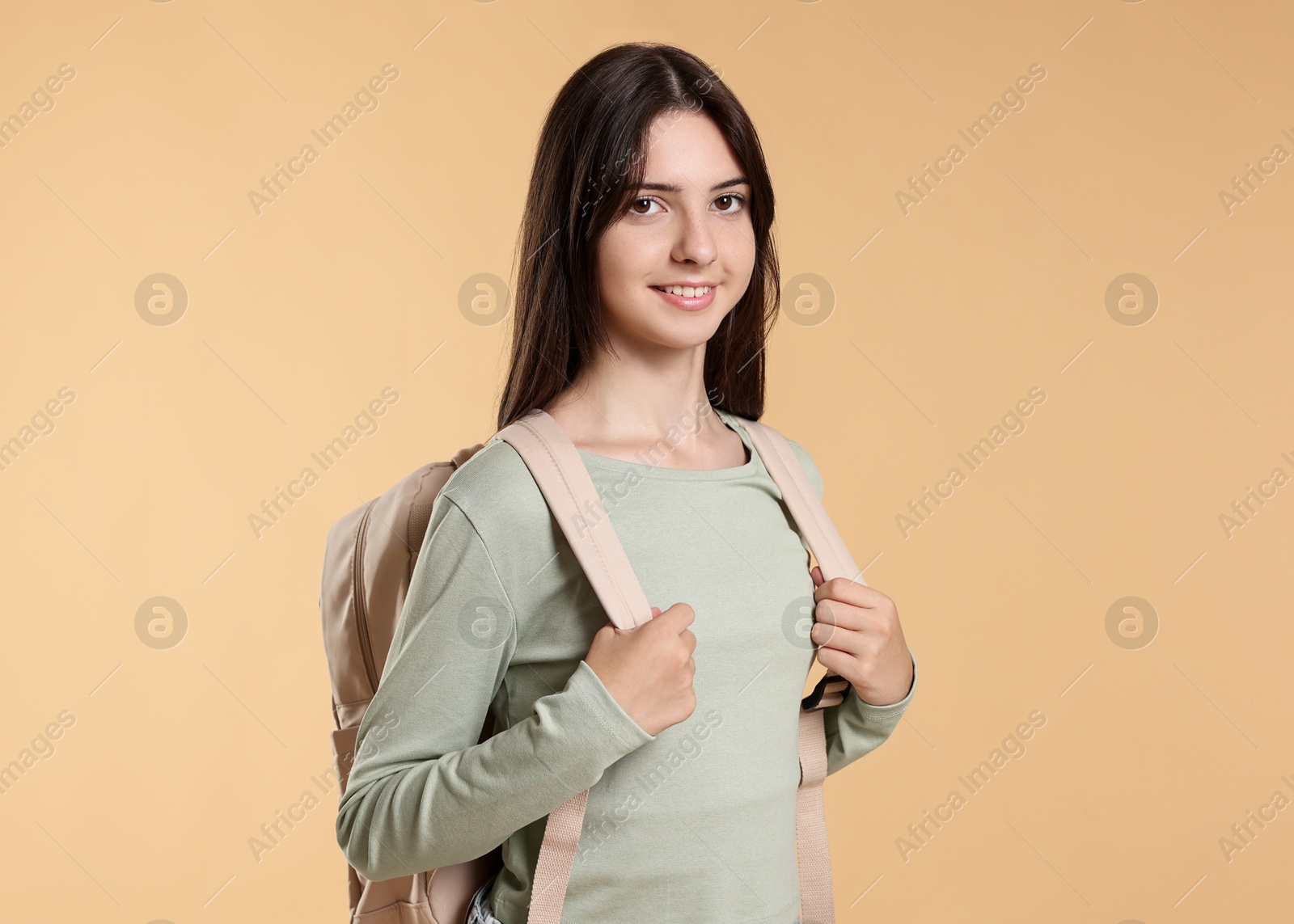 Photo of Portrait of smiling teenage girl with backpack on beige background