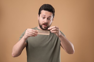 Photo of Emotional man taking his lost hair from comb on beige background. Alopecia problem