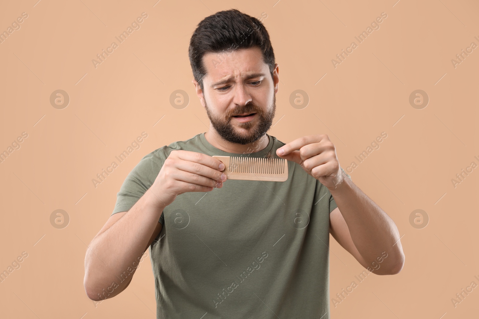 Photo of Sad man taking his lost hair from comb on beige background. Alopecia problem