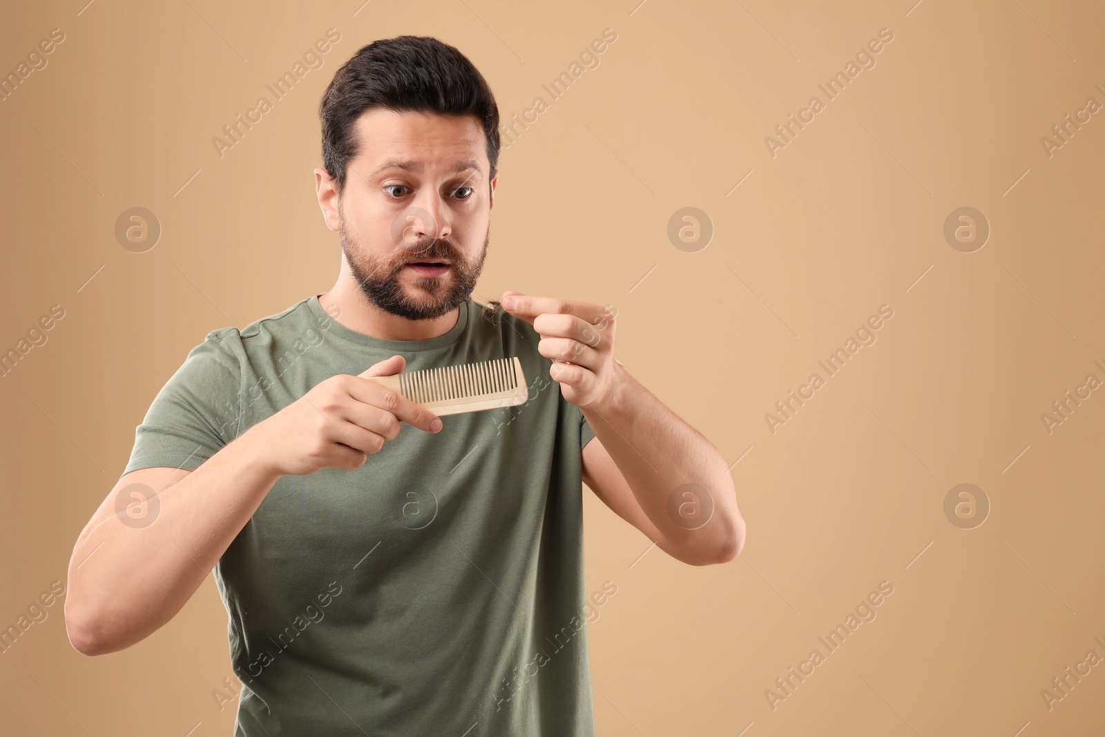 Photo of Emotional man taking her lost hair from comb on beige background, space for text. Alopecia problem