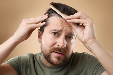 Man brushing his hair on beige background. Alopecia problem