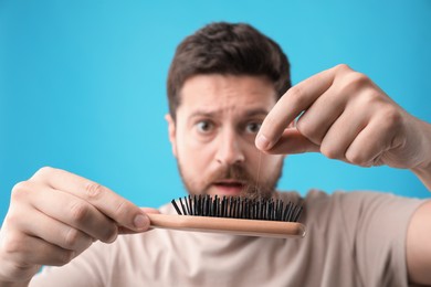 Photo of Emotional man taking his lost hair from brush on light blue background, selective focus. Alopecia problem