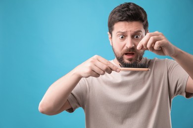 Photo of Emotional man taking his lost hair from brush on light blue background, space for text. Alopecia problem