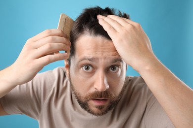 Photo of Man brushing his hair on light blue background. Alopecia problem