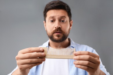 Sad man holding comb with lost hair on gray background, selective focus. Alopecia problem